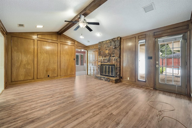 1111 Lupine Dr, Garland, TX 75043 - unfurnished living room with a ceiling fan, light wood-style floors, wood walls, a textured ceiling, and a stone fireplace