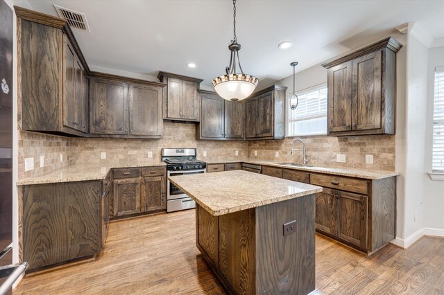 320 Collins St, Argyle, TX 76226 - kitchen with stainless steel gas stove, a sink, light wood-style floors, a kitchen island, and decorative backsplash