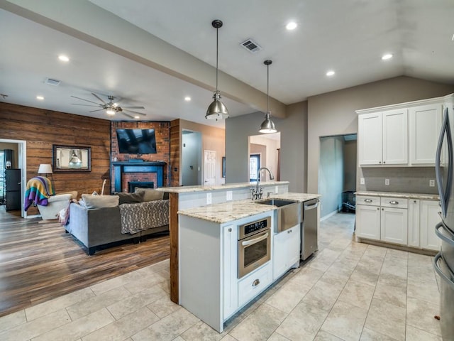 605 Lakeridge Dr, Lavon, TX 75166 - kitchen with stainless steel appliances, ceiling fan, wooden walls, white cabinetry, and a fireplace