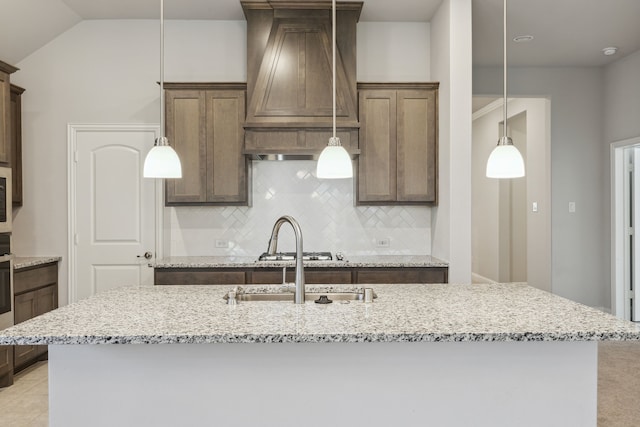 548 Bradley Dr, Fate, TX 75087 - kitchen featuring tasteful backsplash, light stone counters, wall chimney exhaust hood, a kitchen island with sink, and lofted ceiling