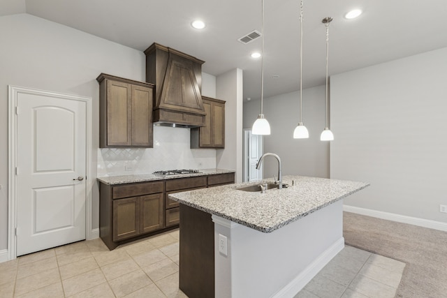 548 Bradley Dr, Fate, TX 75087 - kitchen with custom range hood, a sink, light stone counters, stainless steel gas stovetop, and an island with sink