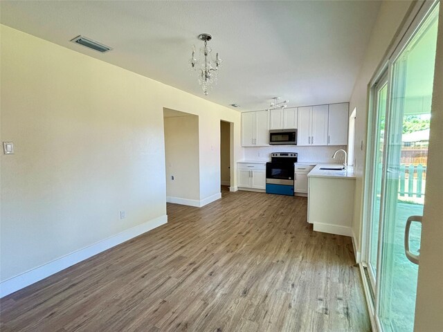 1153 Tracy Ln, Lancaster, TX 75134 - kitchen featuring appliances with stainless steel finishes, a sink, light wood finished floors, a chandelier, and white cabinets