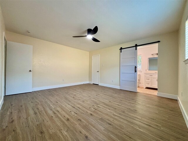 1153 Tracy Ln, Lancaster, TX 75134 - unfurnished bedroom featuring a barn door, wood finished floors, baseboards, ensuite bathroom, and ceiling fan