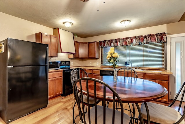 2606 Cedar Elm Ln, Garland, TX 75043 - kitchen featuring black appliances, light wood-style floors, brown cabinetry, wall chimney range hood, and a sink