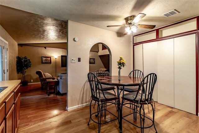2606 Cedar Elm Ln, Garland, TX 75043 - dining room with arched walkways, a textured ceiling, lofted ceiling, light wood finished floors, and a ceiling fan