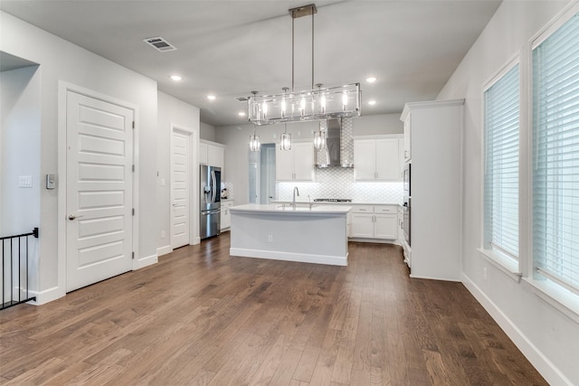 8230 Callimont Ln, Dallas, TX 75231 - kitchen featuring appliances with stainless steel finishes, wall chimney range hood, a sink, a kitchen island with sink, and white cabinets
