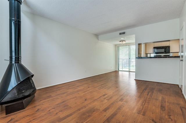 4211 Holland Ave Unit 206, Dallas, TX 75219 - unfurnished living room featuring wood finished floors, a wood stove, a textured ceiling, and baseboards
