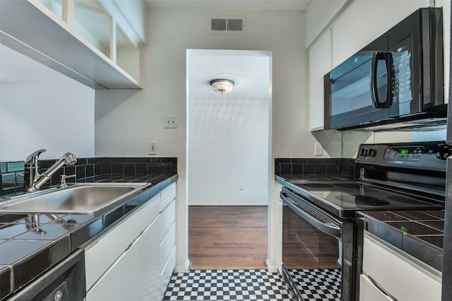 4211 Holland Ave Unit 206, Dallas, TX 75219 - kitchen with black appliances, tile patterned floors, a sink, white cabinets, and tile counters