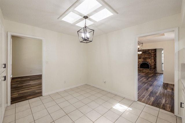 spare room featuring a chandelier, a skylight, a fireplace, light tile patterned floors, and baseboards