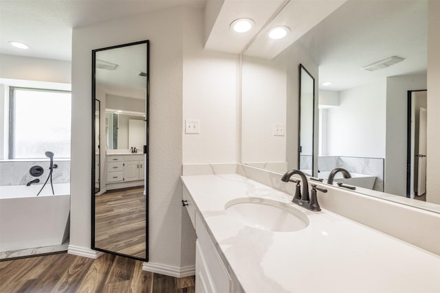 full bath featuring a freestanding tub, wood finished floors, vanity, baseboards, and recessed lighting