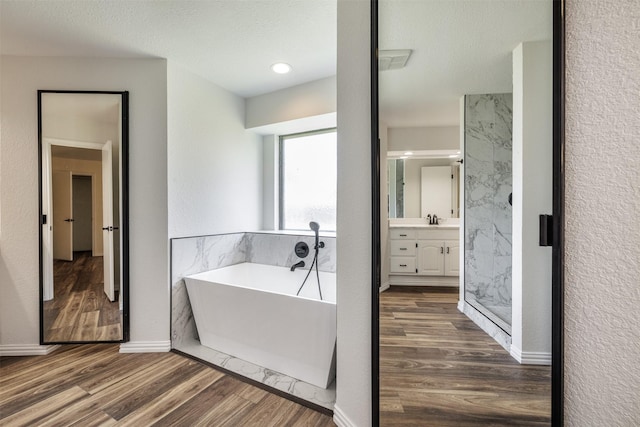 full bath featuring wood finished floors, a soaking tub, vanity, and a marble finish shower
