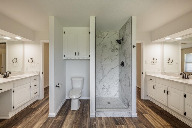 full bathroom featuring a marble finish shower, two vanities, toilet, wood finished floors, and baseboards