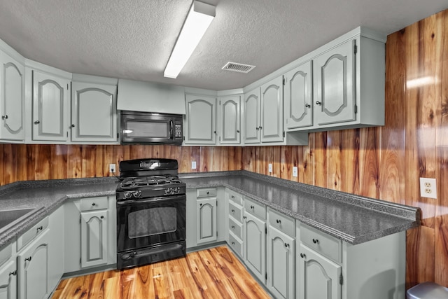 560 N Cardinal Rd, Reno, TX 76020 - kitchen featuring black appliances, a textured ceiling, dark countertops, light wood-style flooring, and wooden walls