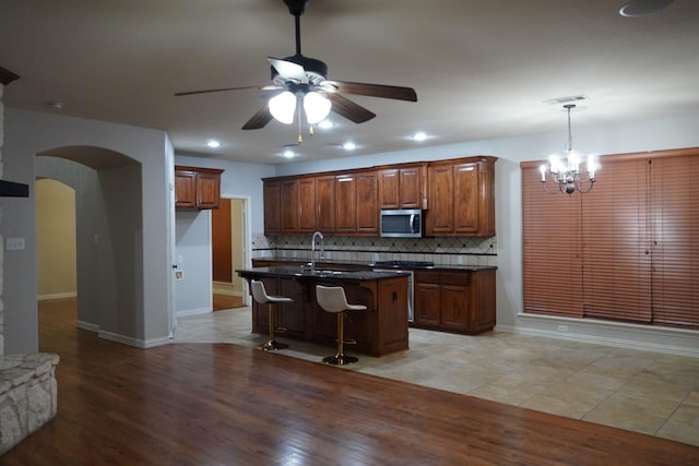 1136 Philip Dr, Allen, TX 75013 - kitchen featuring stainless steel microwave, a ceiling fan, dark countertops, arched walkways, and backsplash
