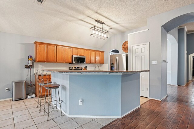 5729 Brazos Dr, Haltom City, TX 76137 - kitchen featuring stainless steel appliances, arched walkways, lofted ceiling, a textured ceiling, and baseboards