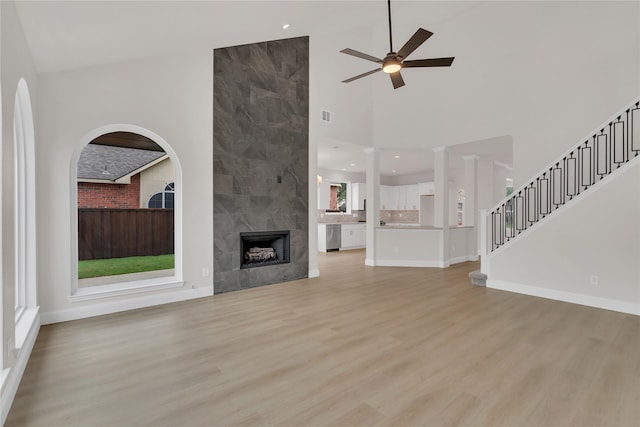 1529 Harvest Run Dr, Allen, TX 75002 - unfurnished living room featuring a ceiling fan, light wood-type flooring, a tile fireplace, a high ceiling, and stairs