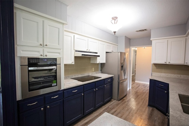 1413 Oak Hills Dr, Graham, TX 76450 - kitchen featuring stainless steel appliances, under cabinet range hood, blue cabinets, tasteful backsplash, and light wood-style flooring