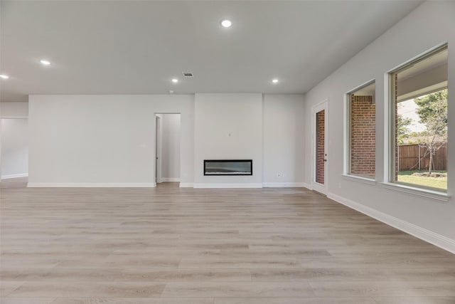 7111 Manhattan Dr, Rowlett, TX 75088 - unfurnished living room featuring light wood-style flooring, recessed lighting, a glass covered fireplace, and baseboards