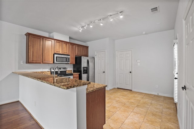5719 Butterfly Way, Fairview, TX 75069 - kitchen featuring stainless steel appliances, brown cabinetry, a peninsula, dark stone countertops, and rail lighting