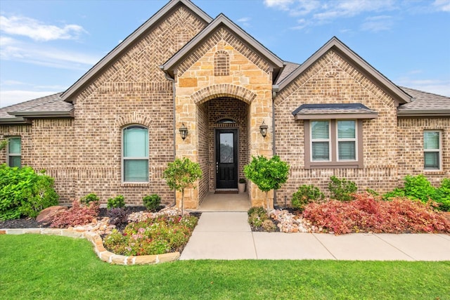 french country home featuring brick siding, a shingled roof, and stone siding