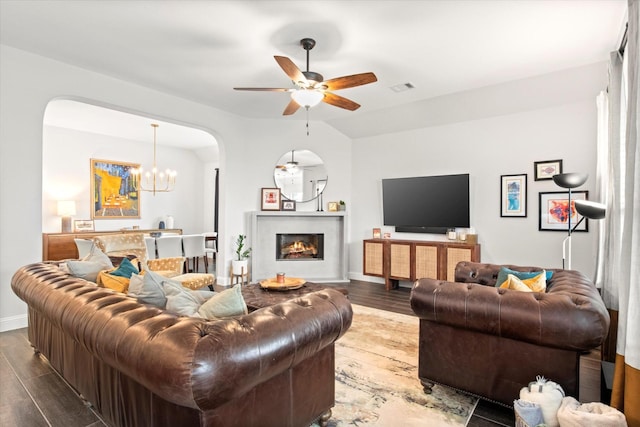 living area with wood finished floors, ceiling fan, a chandelier, and a lit fireplace