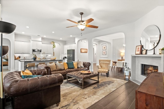living room featuring a ceiling fan, dark wood finished floors, arched walkways, recessed lighting, and a fireplace