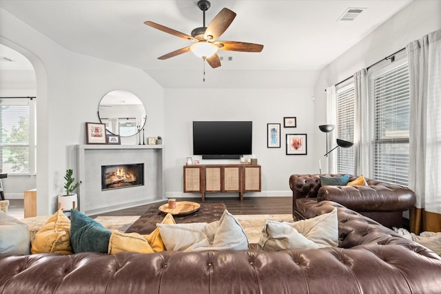 living room featuring wood finished floors, arched walkways, healthy amount of natural light, ceiling fan, and vaulted ceiling