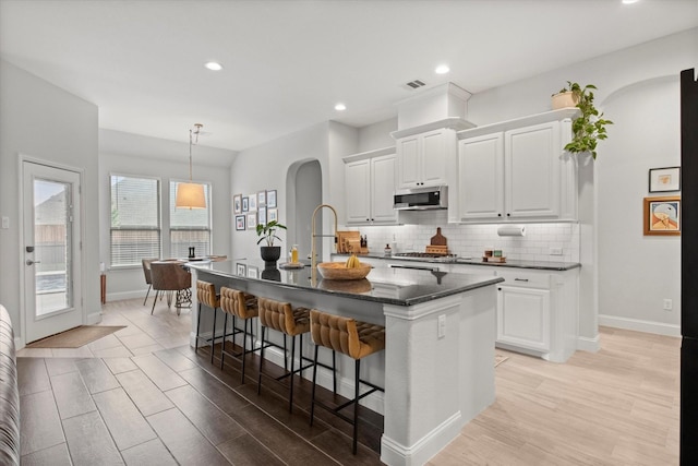 kitchen featuring stainless steel appliances, arched walkways, baseboards, light wood-type flooring, and recessed lighting