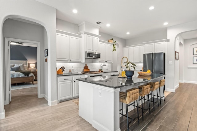kitchen with stainless steel appliances, arched walkways, a breakfast bar, baseboards, and light wood-type flooring