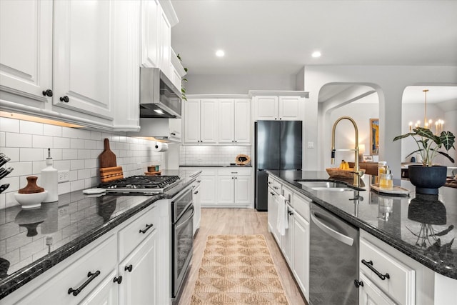 kitchen with appliances with stainless steel finishes, a sink, arched walkways, white cabinets, and recessed lighting
