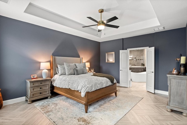 bedroom with a tray ceiling, baseboards, ensuite bathroom, and ceiling fan