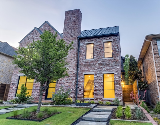 contemporary home featuring a standing seam roof, brick siding, a chimney, and fence