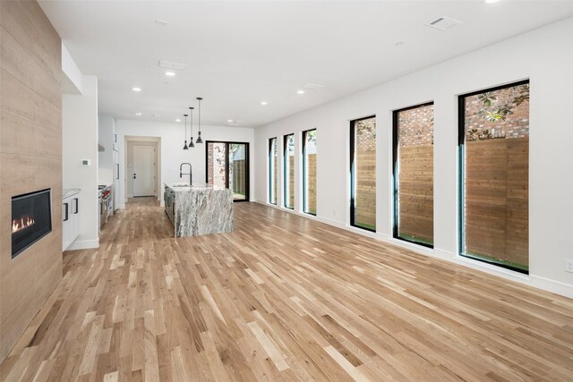 unfurnished living room with a sink, light wood-type flooring, a tiled fireplace, recessed lighting, and baseboards