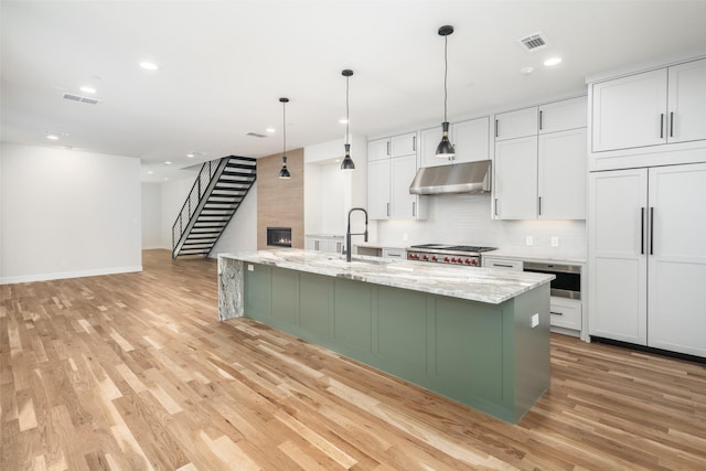 kitchen featuring a sink, under cabinet range hood, light wood-style floors, baseboards, and white cabinetry