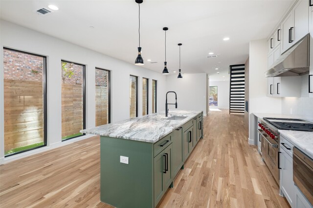 kitchen featuring a sink, under cabinet range hood, light wood-style floors, white cabinets, and recessed lighting