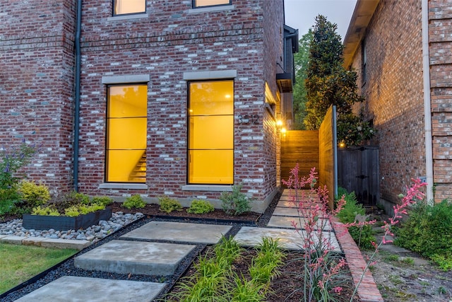 view of exterior entry featuring brick siding and fence