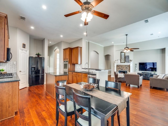 1710 Redcedar Dr, Wylie, TX 75098 - dining space with a ceiling fan, a stone fireplace, arched walkways, recessed lighting, and dark wood-type flooring