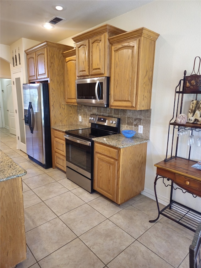 16 Cedar Bayou Cir, Pottsboro, TX 75076 - kitchen featuring appliances with stainless steel finishes, light stone countertops, backsplash, light tile patterned flooring, and brown cabinetry