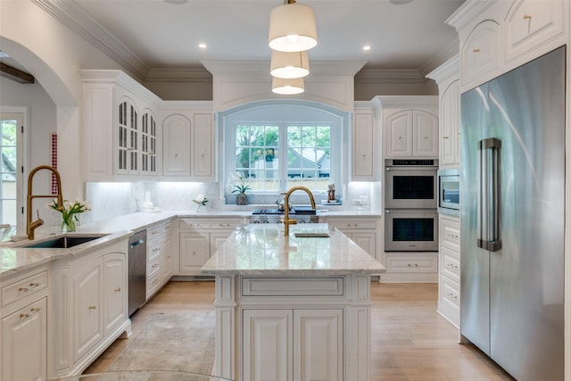 kitchen featuring appliances with stainless steel finishes, a sink, healthy amount of natural light, light stone countertops, and crown molding