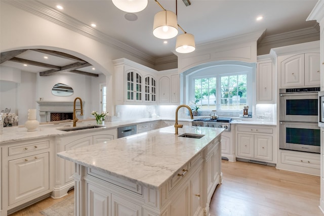 kitchen with a sink, appliances with stainless steel finishes, arched walkways, a center island with sink, and recessed lighting