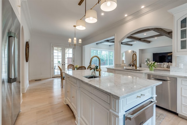 kitchen with a sink, stainless steel appliances, arched walkways, beam ceiling, and a kitchen island with sink