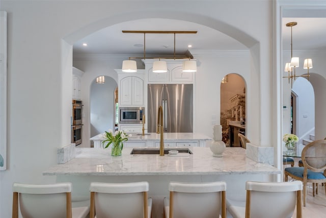 kitchen featuring stainless steel appliances, a sink, a peninsula, arched walkways, and white cabinets