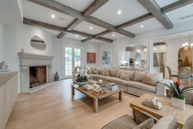 living room featuring arched walkways, coffered ceiling, light wood finished floors, beam ceiling, and a fireplace with raised hearth