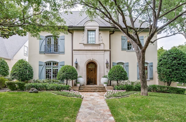 view of front of home featuring stucco siding, a front yard, and a balcony