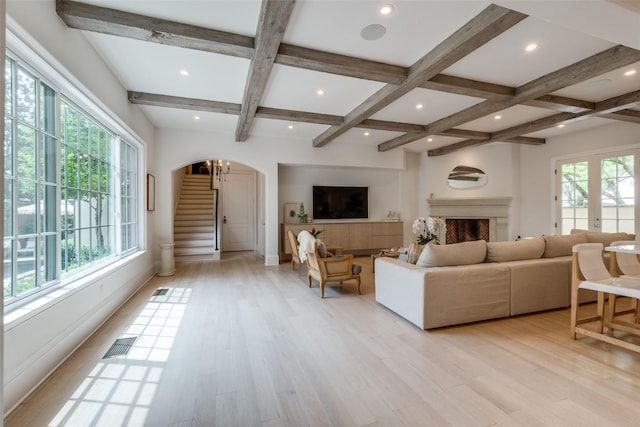 living area featuring coffered ceiling, arched walkways, stairs, light wood-type flooring, and beamed ceiling