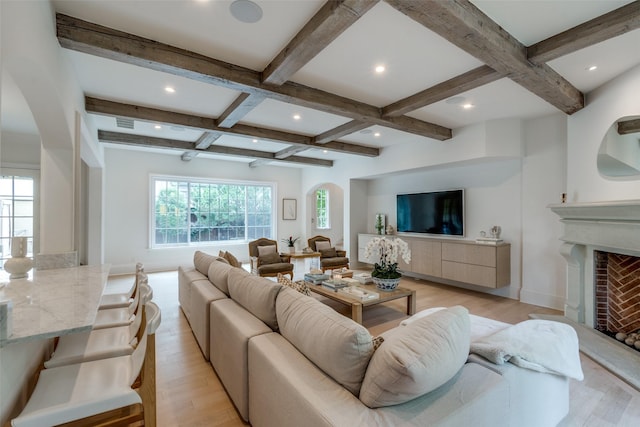 living room featuring coffered ceiling, arched walkways, beam ceiling, light wood finished floors, and a fireplace