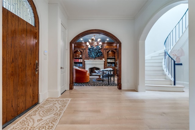 foyer entrance with arched walkways, stairway, wood finished floors, a chandelier, and baseboards