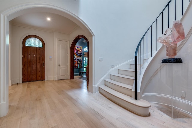 entrance foyer featuring arched walkways, light wood finished floors, stairway, crown molding, and baseboards