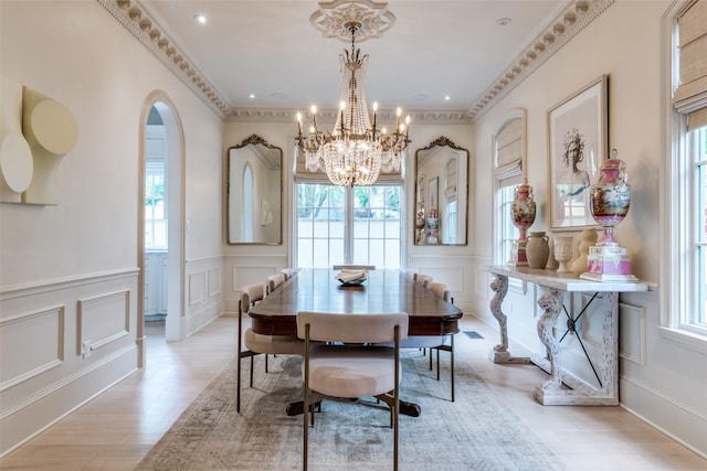 dining area featuring a decorative wall, a chandelier, light wood finished floors, a wainscoted wall, and crown molding