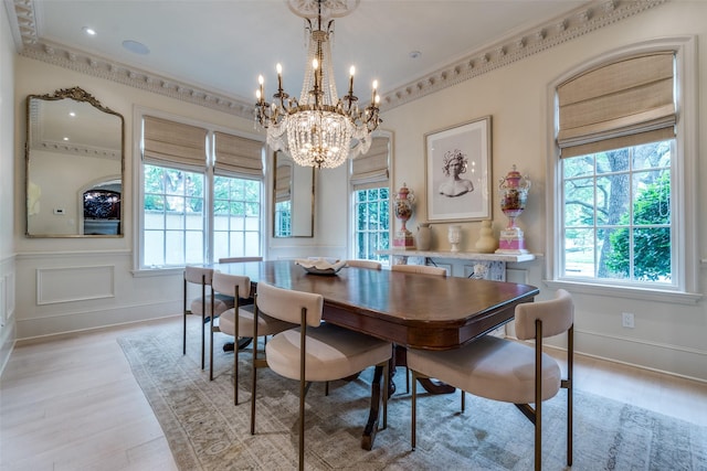 dining room featuring healthy amount of natural light, light wood-style floors, a chandelier, ornamental molding, and a decorative wall